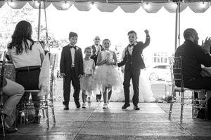 Flower girls and ring bearers walk down aisle in black and white wedding ceremony photo.