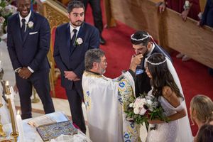 Bride and groom share intimate moment with officiant during church wedding ceremony.