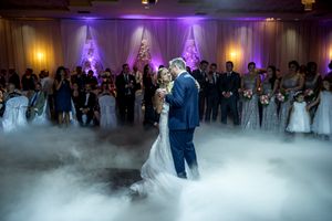 Couple shares first dance on a cloud-filled dance floor with purple lighting at wedding reception.