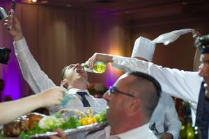 Wedding guest enthusiastically drinks a shot at a lively wedding reception dinner table.