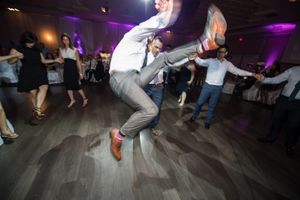Energetic wedding guest performs a high-kick dance move on the reception dance floor.