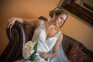 Beautiful bride in lace gown sitting in leather chair holding bouquet of white roses.