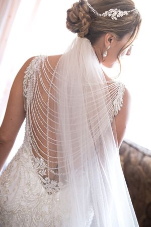 Bride showcasing intricate pearl-draped veil and beaded back wedding dress with updo hairstyle.