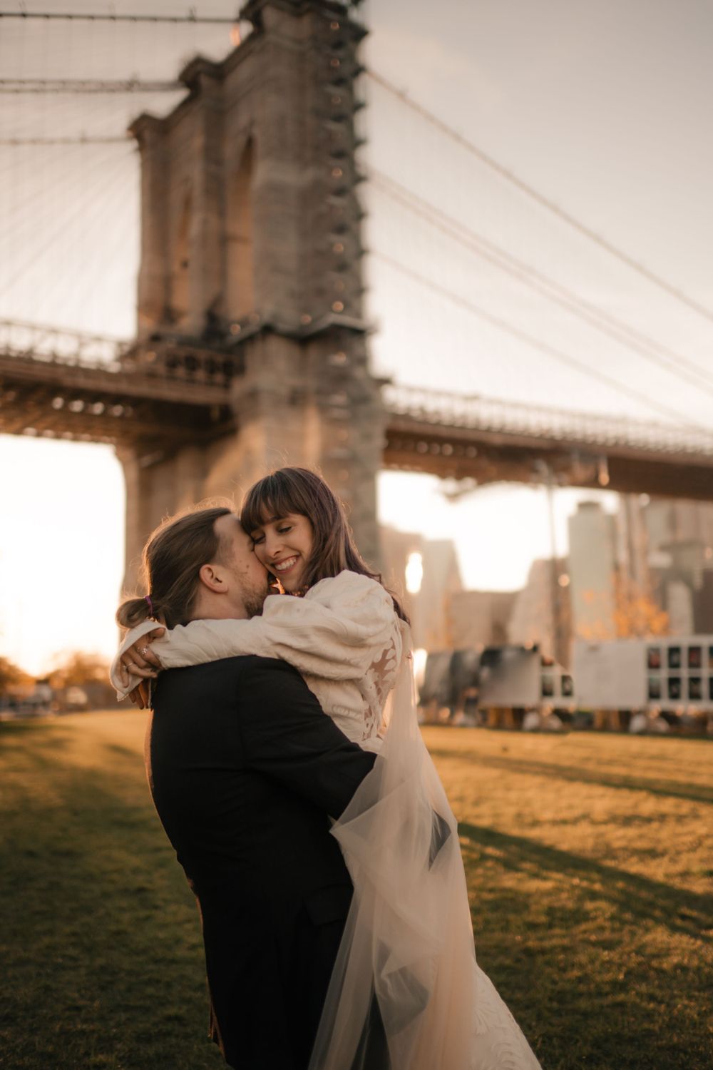 Joyful wedding couple embracing by Brooklyn Bridge during golden hour.