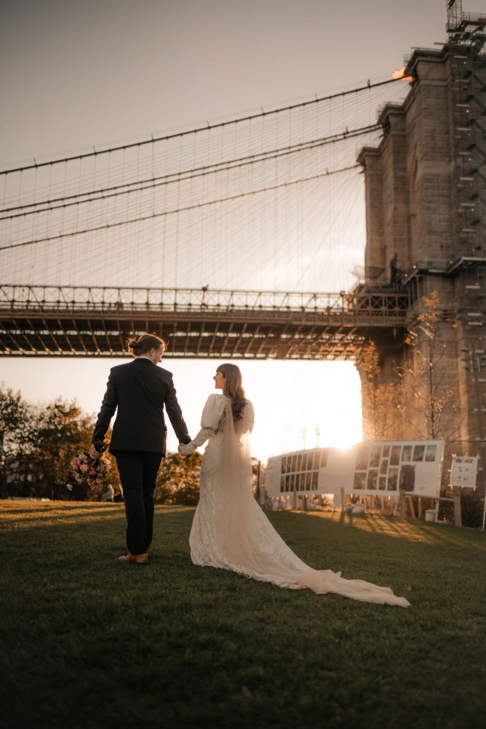 Wedding couple walking hand in hand near Brooklyn Bridge at sunset.