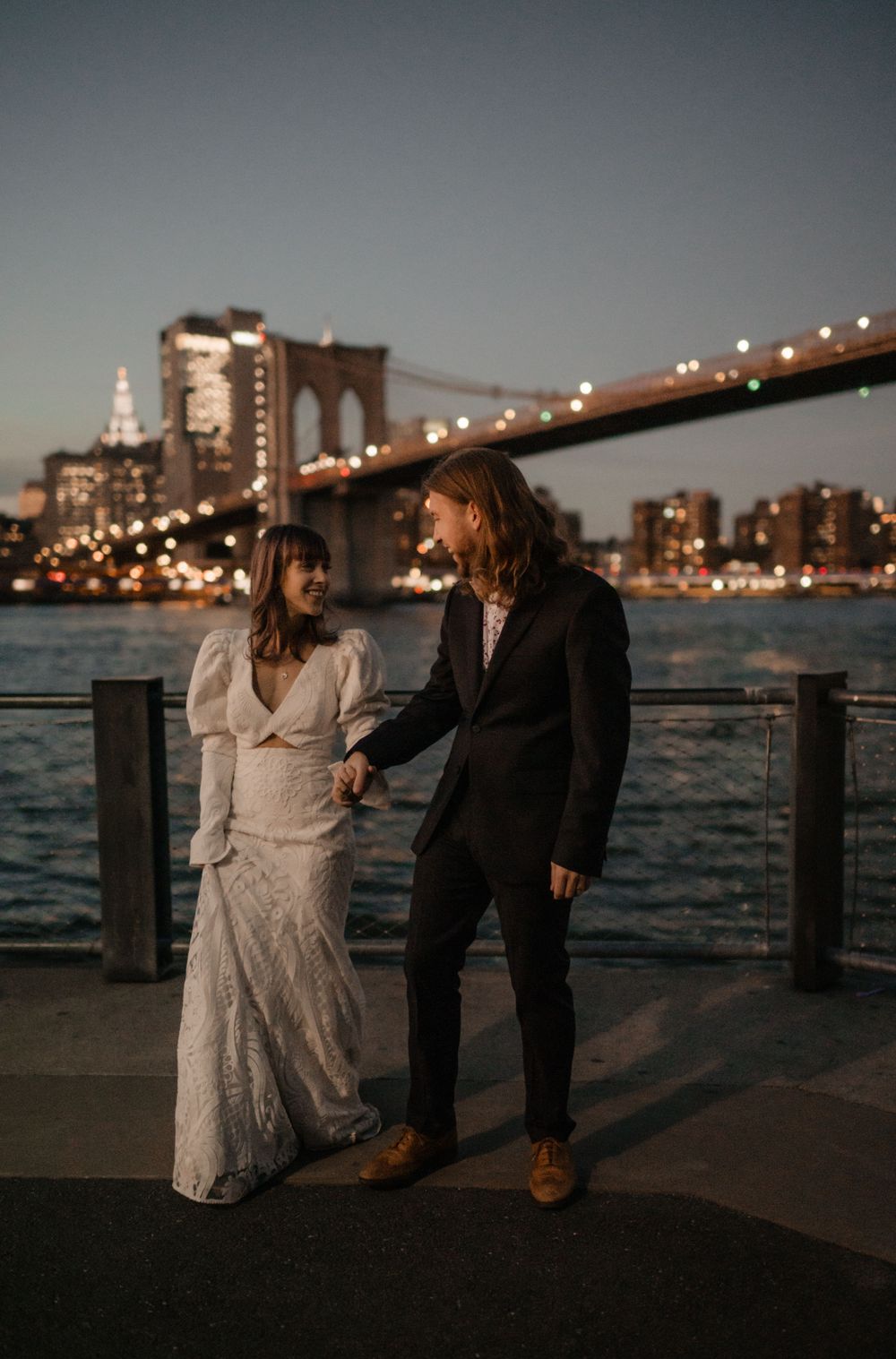 Romantic wedding photo with Brooklyn Bridge and NYC skyline at dusk.