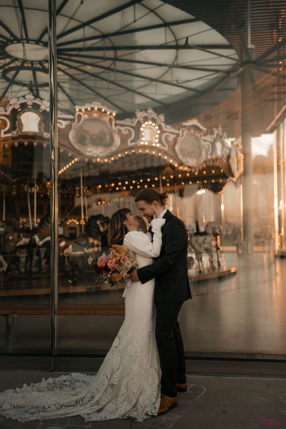 Wedding couple sharing romantic moment by vintage carousel with fairy lights.