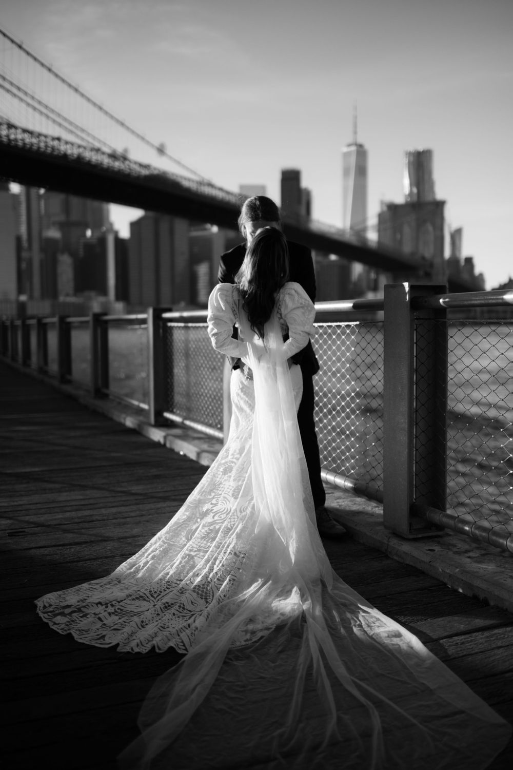 Romantic black and white wedding photo of couple by Brooklyn Bridge with NYC skyline.