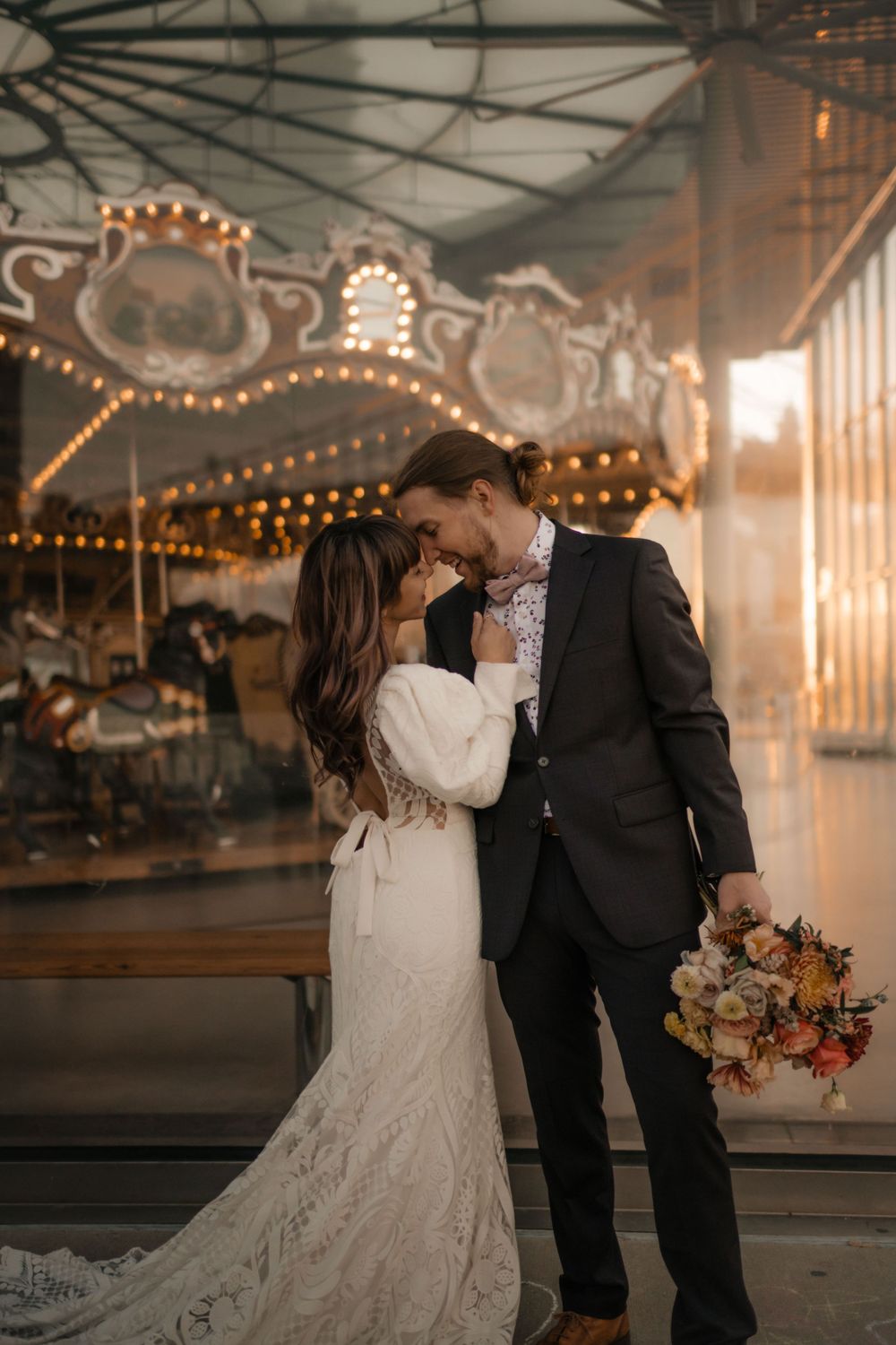 Intimate wedding moment photographed beside an ornate carousel with warm lighting.