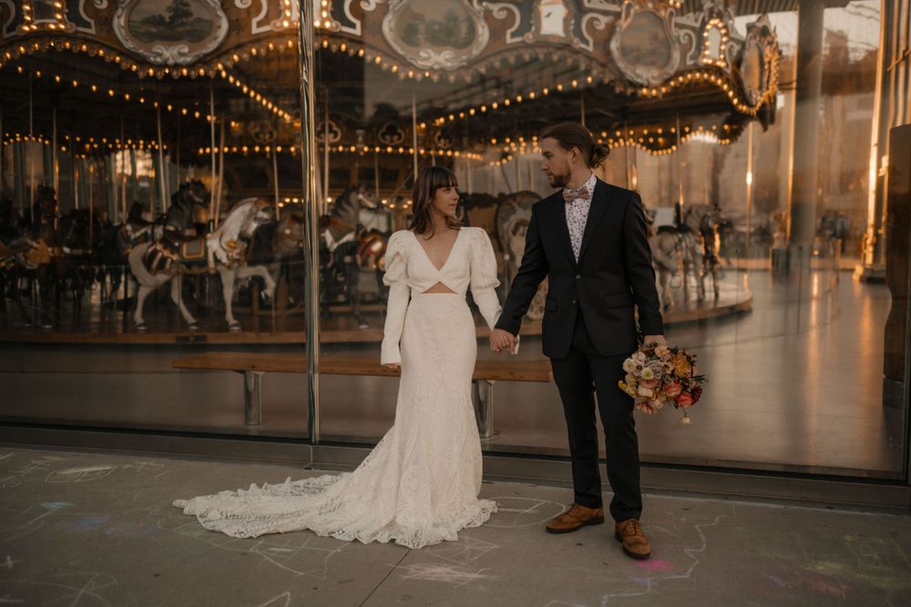 A romantic wedding photo by a vintage carousel with soft lighting and fall-toned florals.