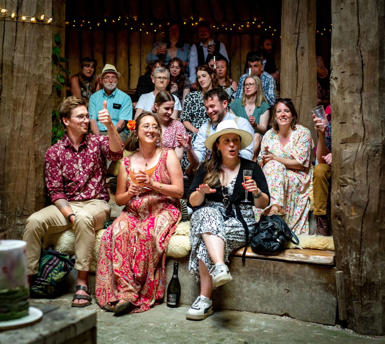 Wedding guests seated and enjoying festivities in rustic barn venue with string lights.
