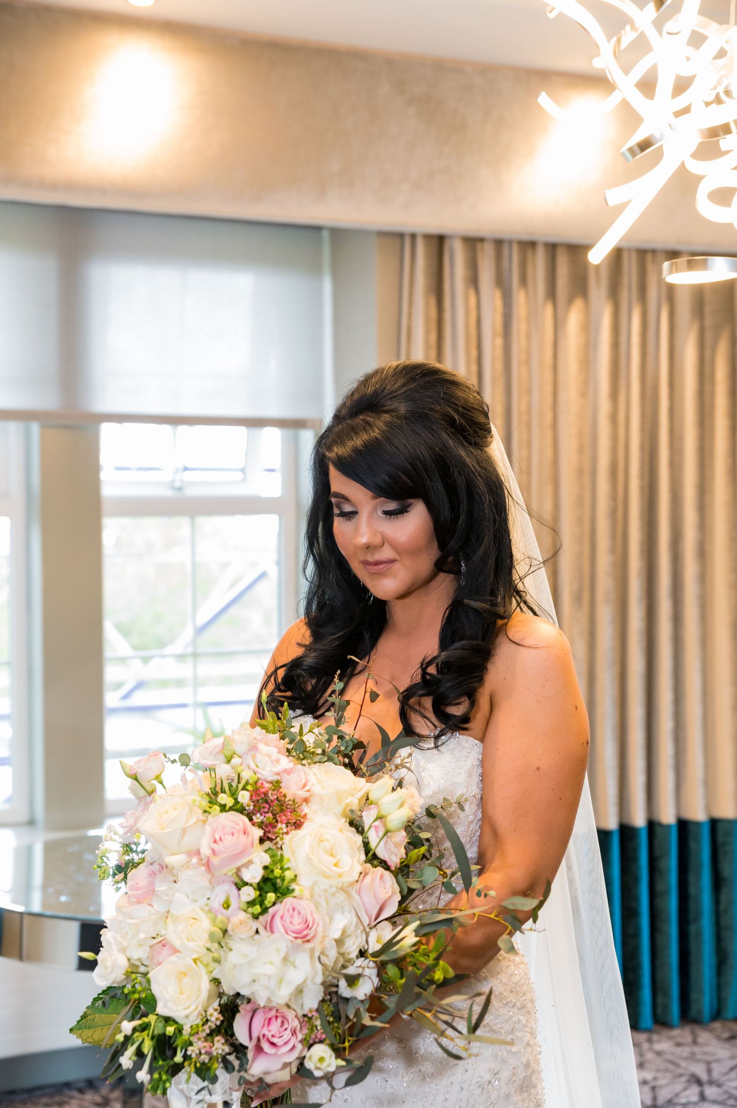 A bride holds an elegant bouquet of pink and white flowers in an indoor setting with modern lighting.