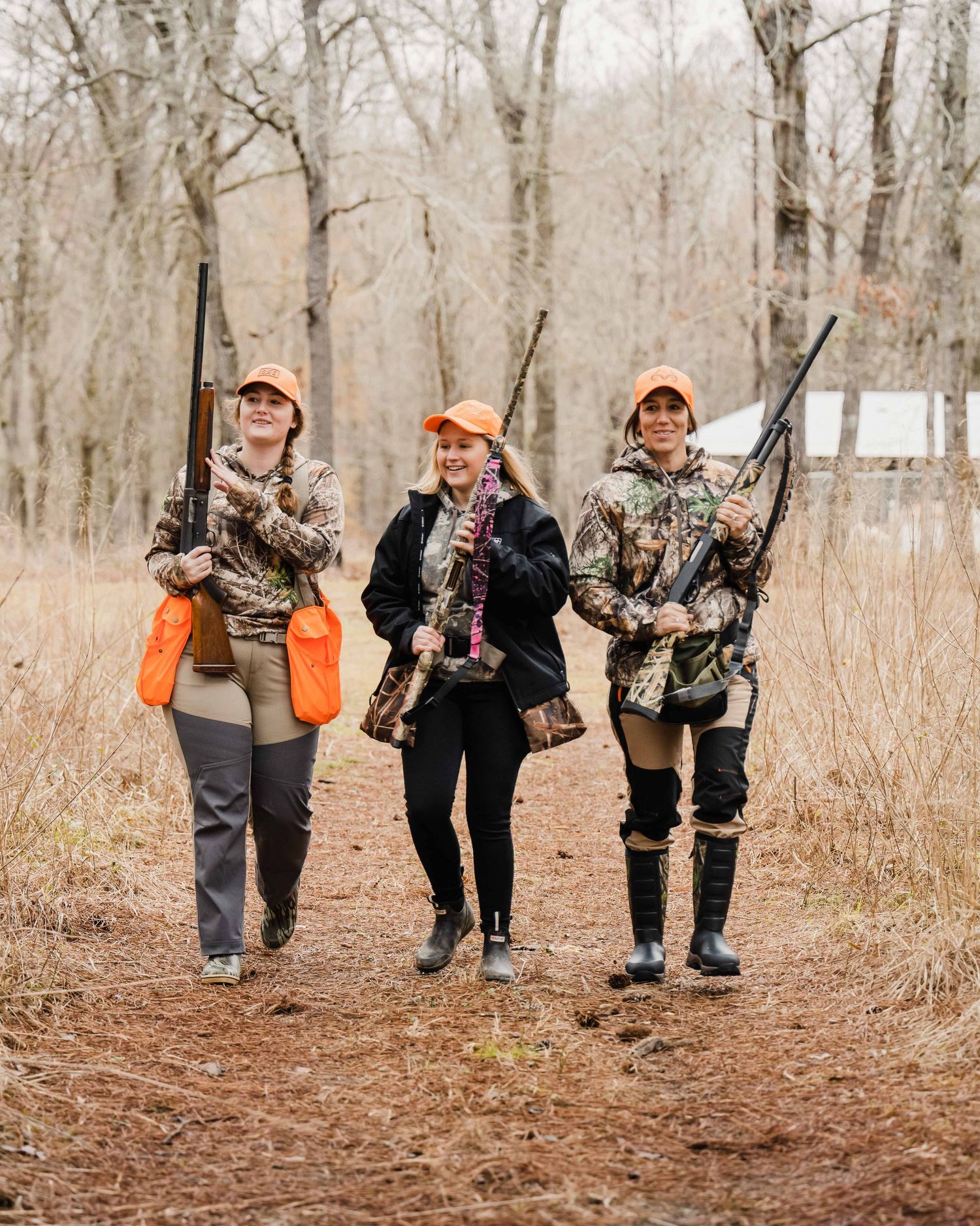 Hunters in orange safety vests and camo gear walking through autumn woods.