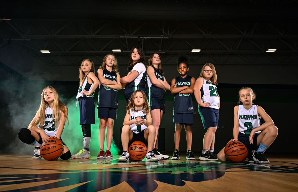 Basketball team members pose with balls on court with dramatic lighting and smoke effects.