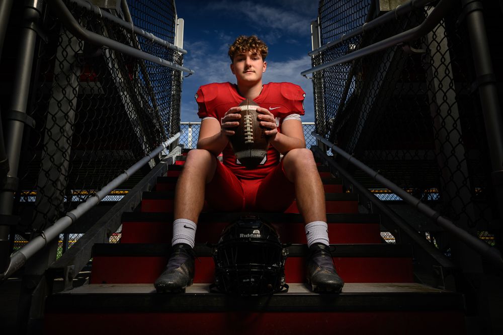 Dramatic low-angle view of a football player sitting on stadium steps wearing red uniform at dusk.