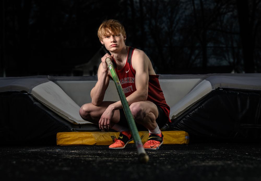 Track athlete sits on equipment in red uniform against dark background.