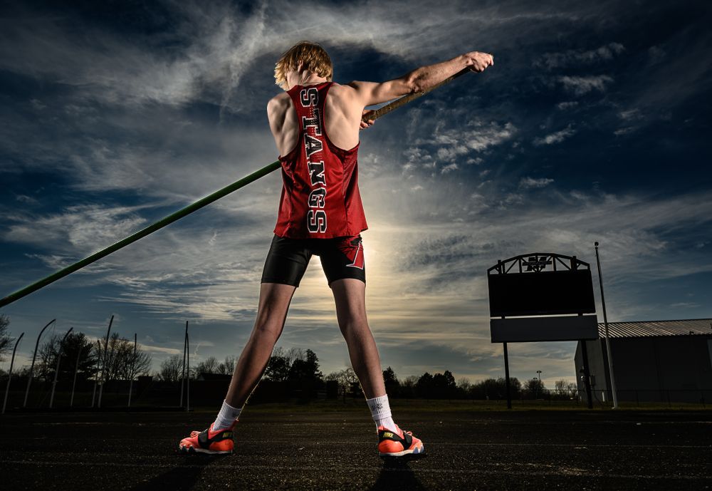 Track and field athlete practices javelin throw against dramatic cloudy sky.