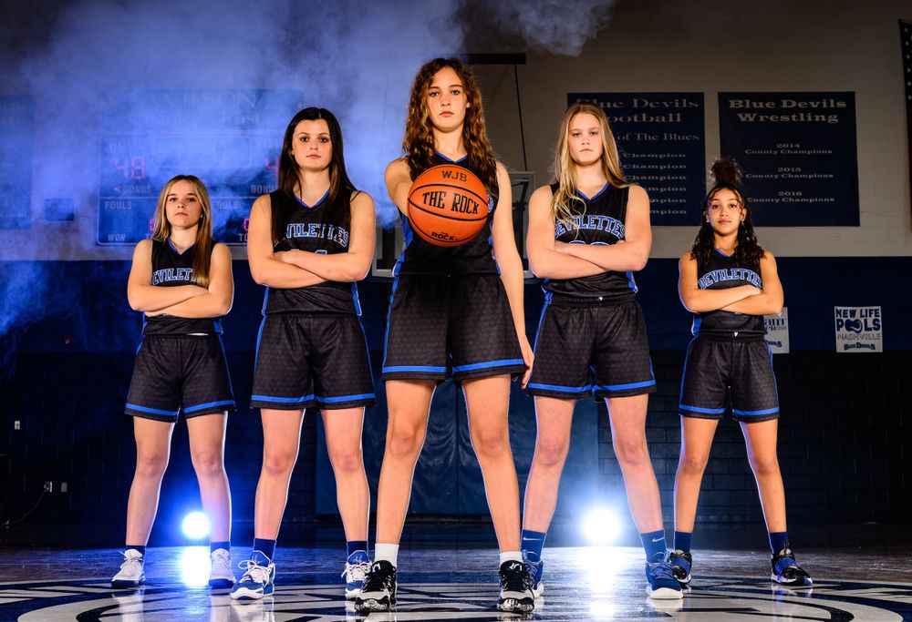 Basketball team poses dramatically with blue lighting effects in gym uniforms.