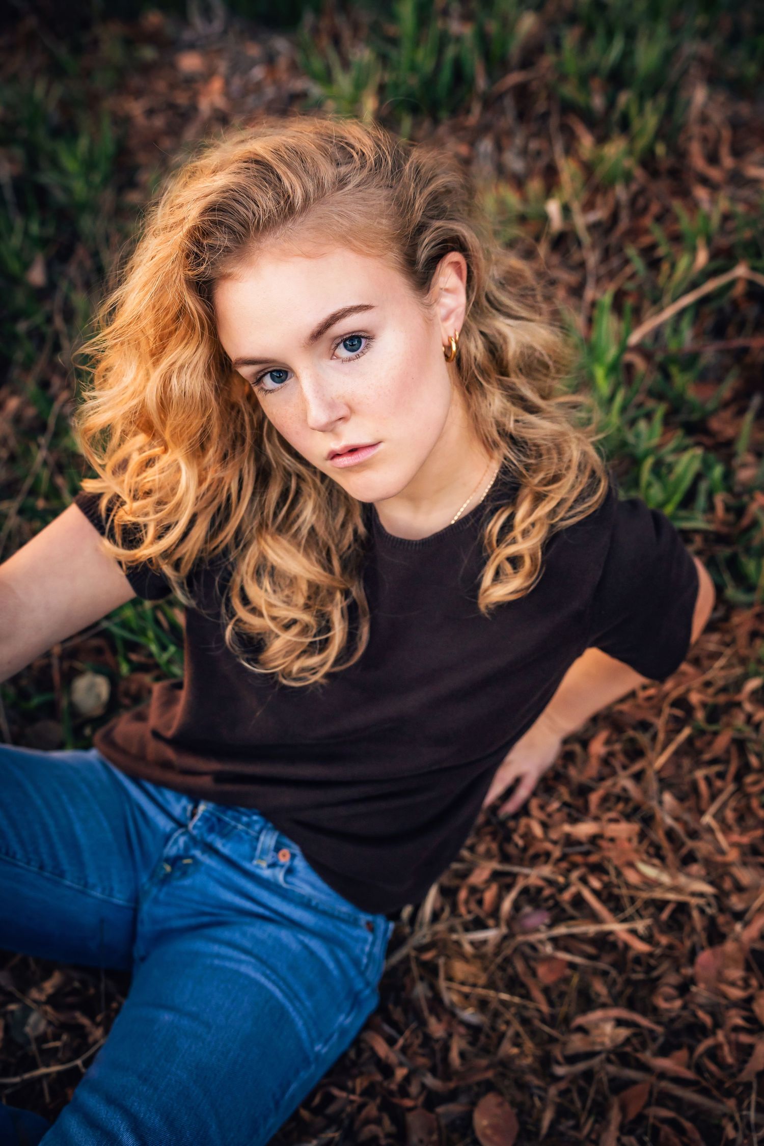 Portrait with flowing blonde curls against natural foliage background.