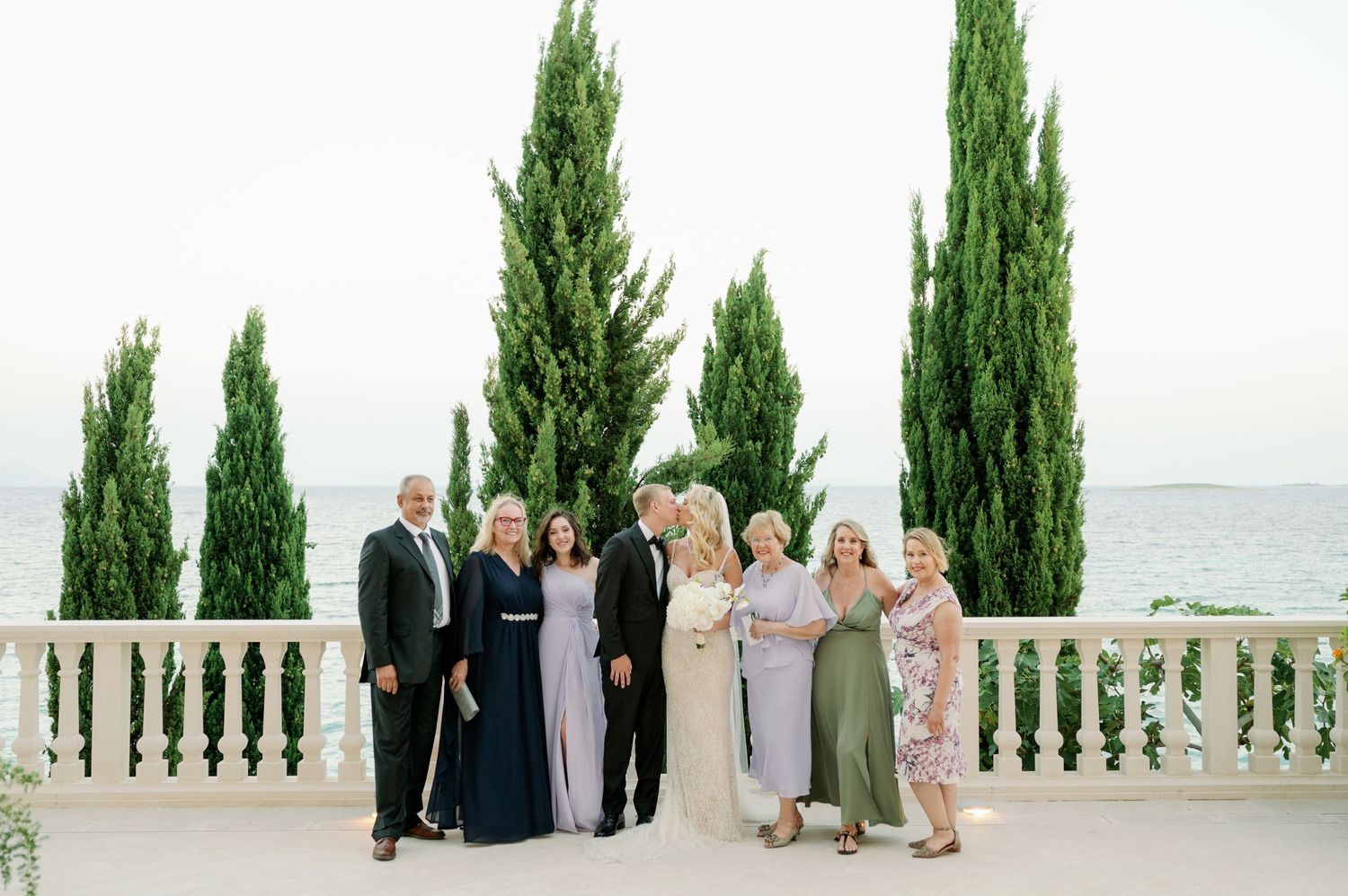 Family group portrait on a Mediterranean terrace with classic white balustrades and cypress trees.