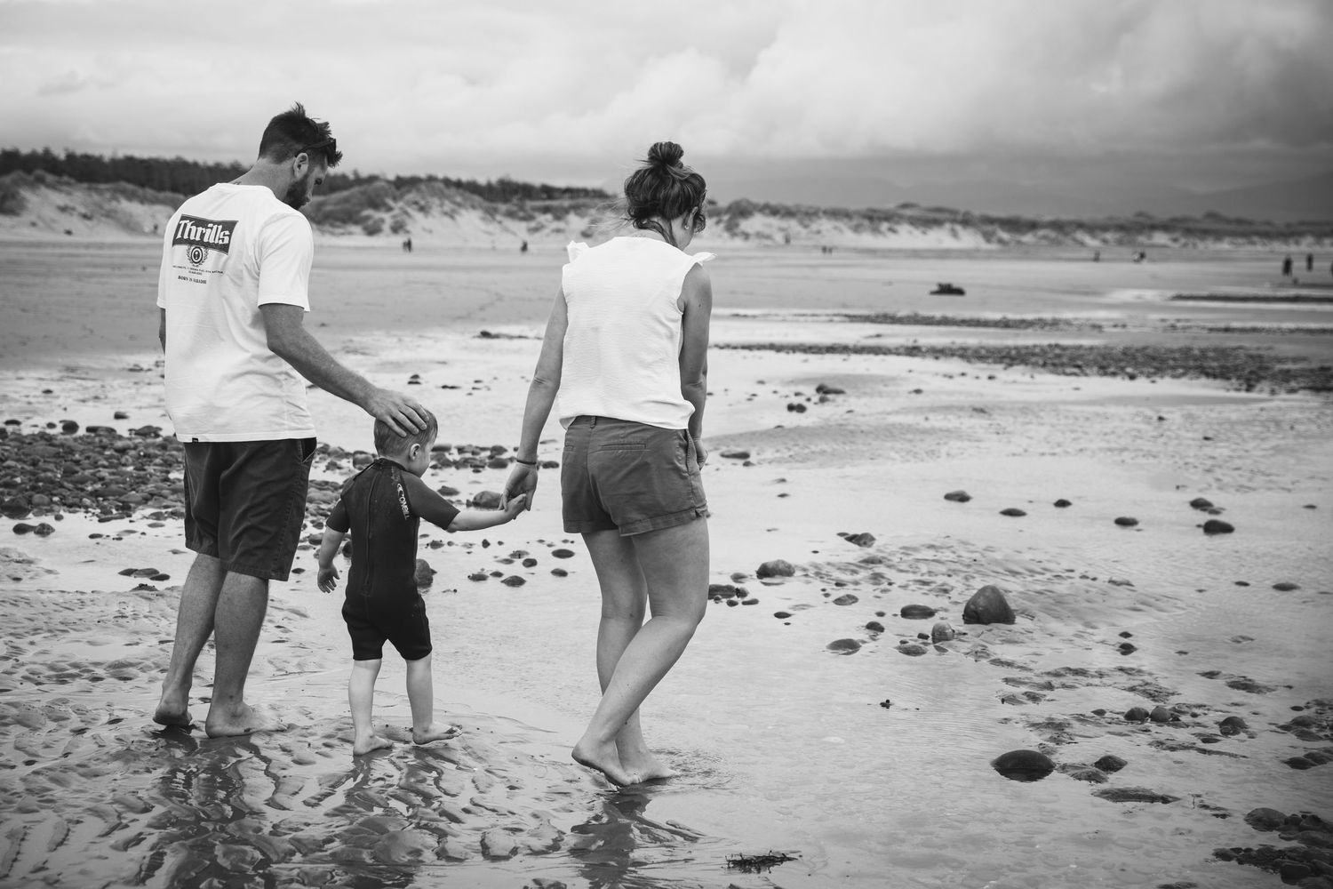 People walking together along shoreline in black and white beach scene.
