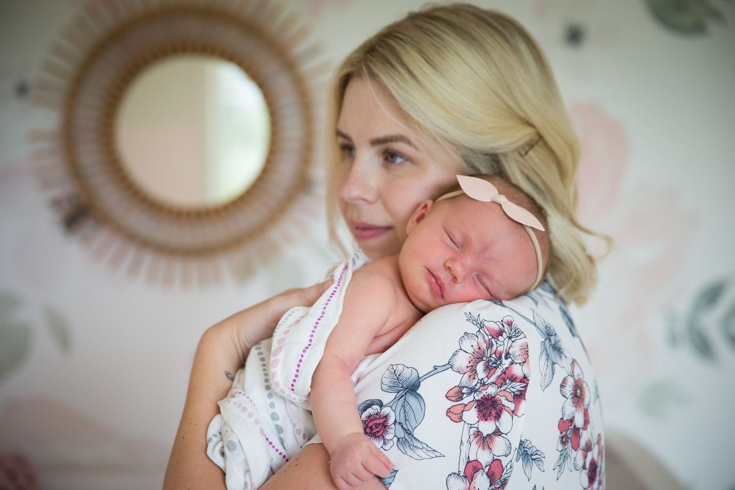newborn baby girl with a bow held by mum in the nursery