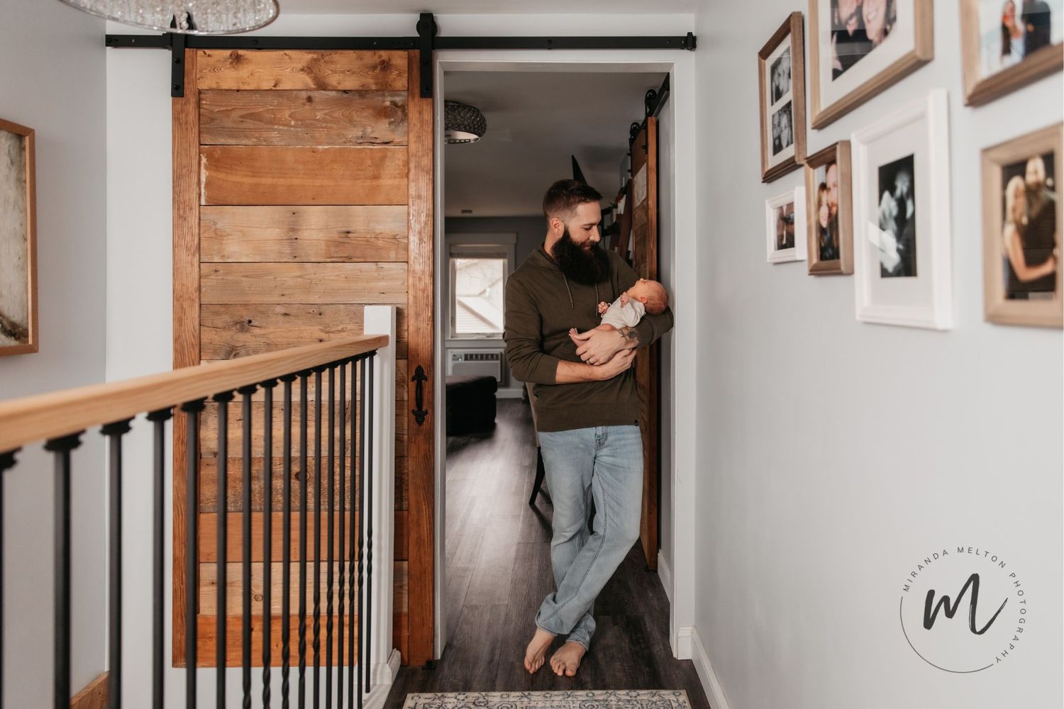 A professional family photo of a father cuddling his newborn son in a rustic doorframe at their home in the Twin Cities