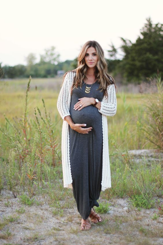 Boho maternity style with long white cardigan and charcoal maxi dress in rustic field setting.