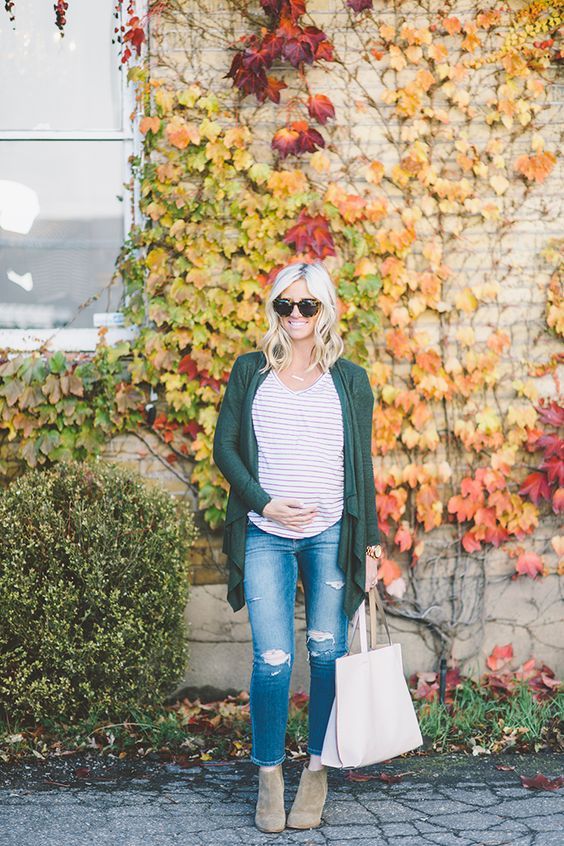 Fall fashion look with striped top, green cardigan and distressed jeans against colorful autumn foliage.