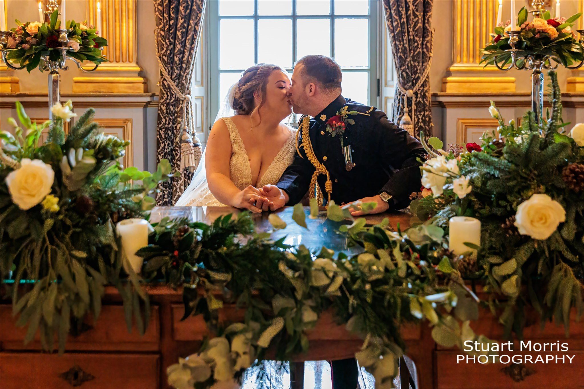 Bride and groom kiss as they sit signing the register. Knowsley hall wedding photographs.