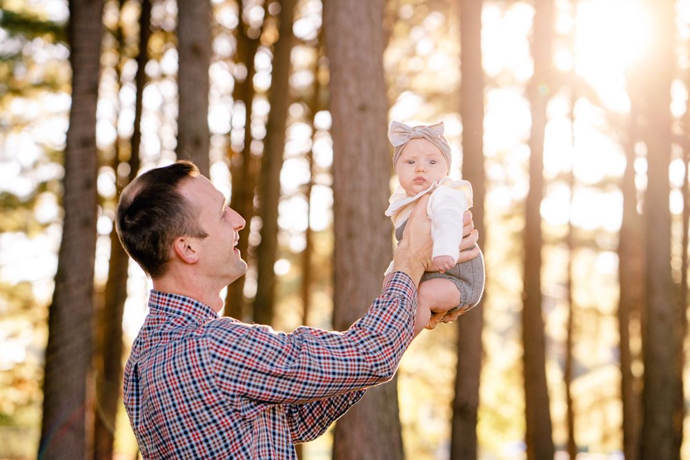 Joyful parenting moment captured in golden sunlight streaming through forest trees.