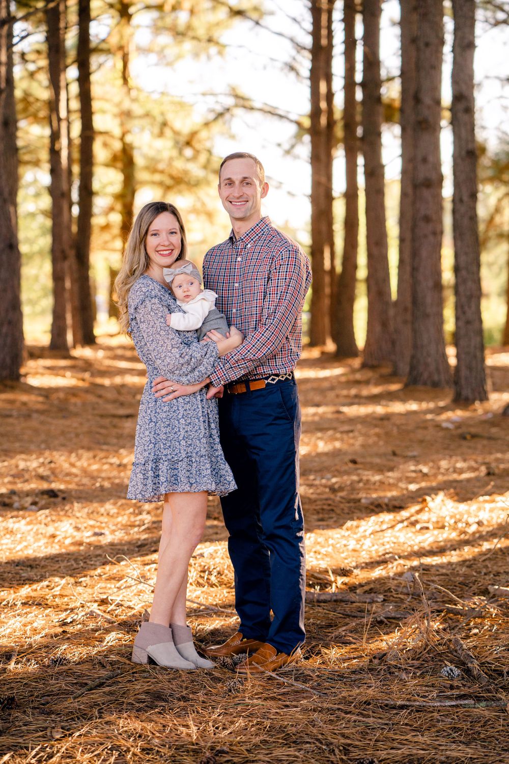 Beautiful family portrait in a pine forest with golden sunlight creating a warm autumn atmosphere.