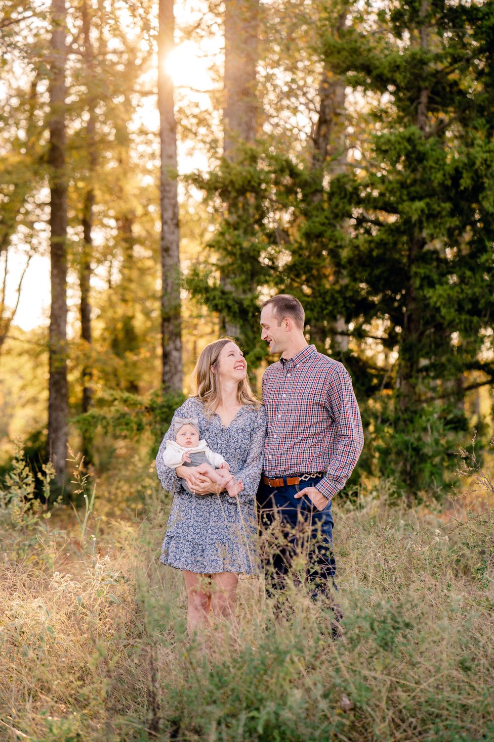 A tender family moment captured in a wooded area during golden hour with sunlight streaming through trees.
