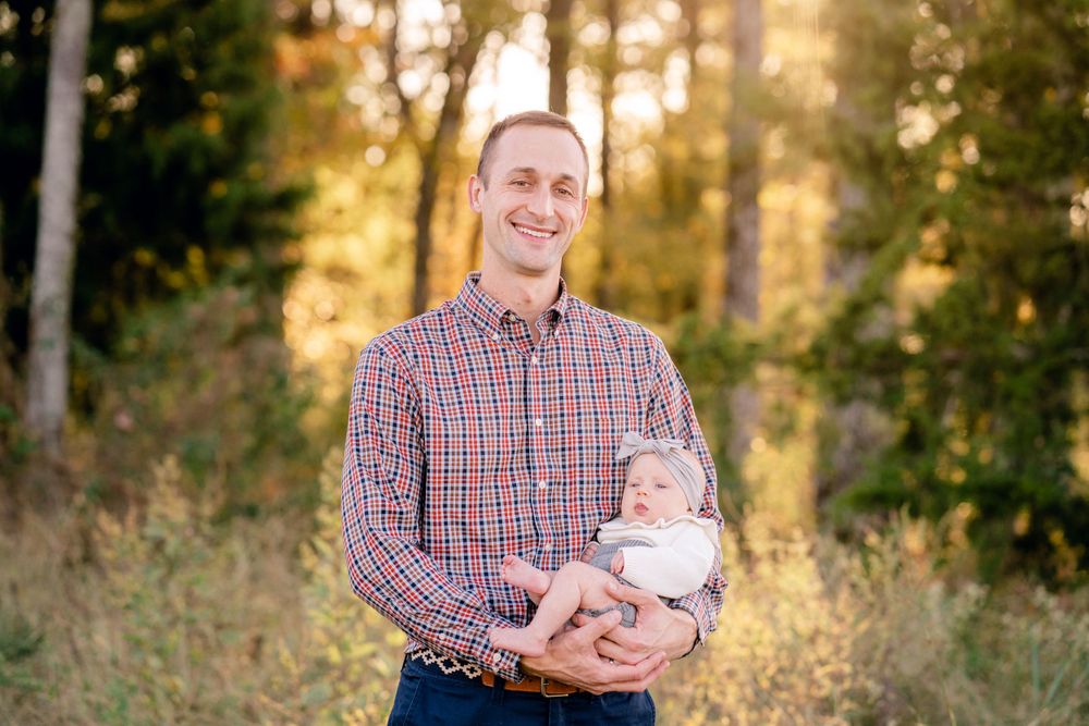 Heartwarming outdoor portrait of parent and baby against a sunlit forest backdrop.
