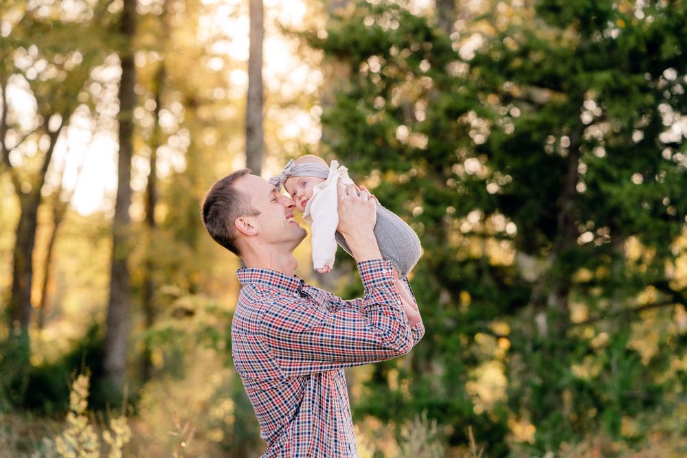 Parent lifting baby up against golden sunlit forest background.
