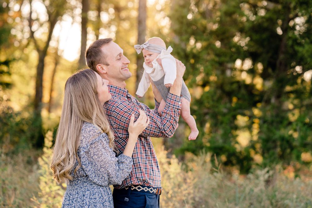 Happy family playing with baby in field during sunset.