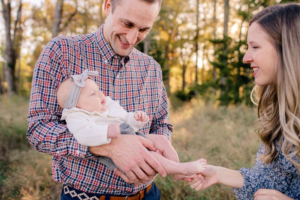 Candid moment of family laughing together while holding baby outdoors.