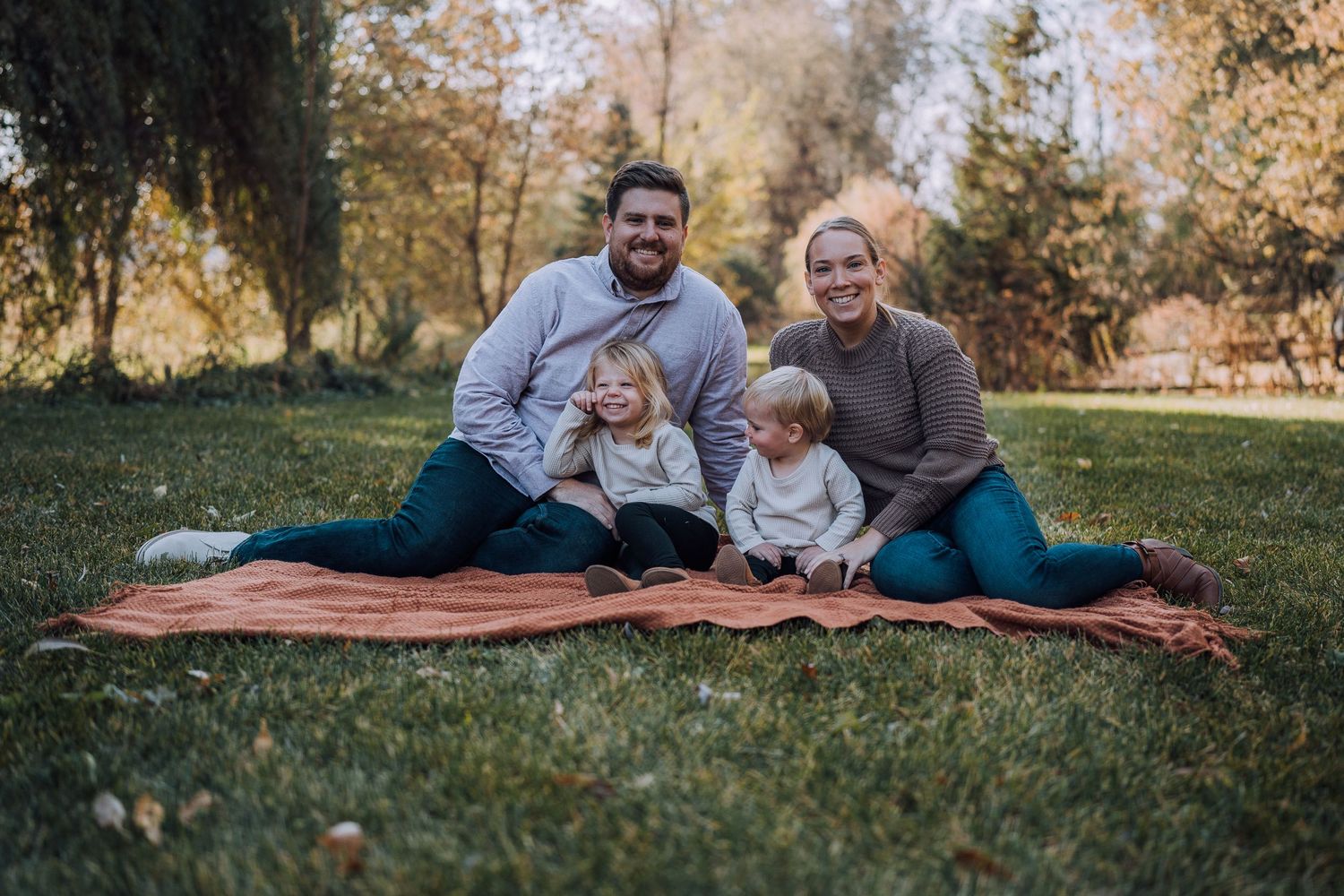 A family enjoys quality time together on a rustic blanket in an autumn park setting.