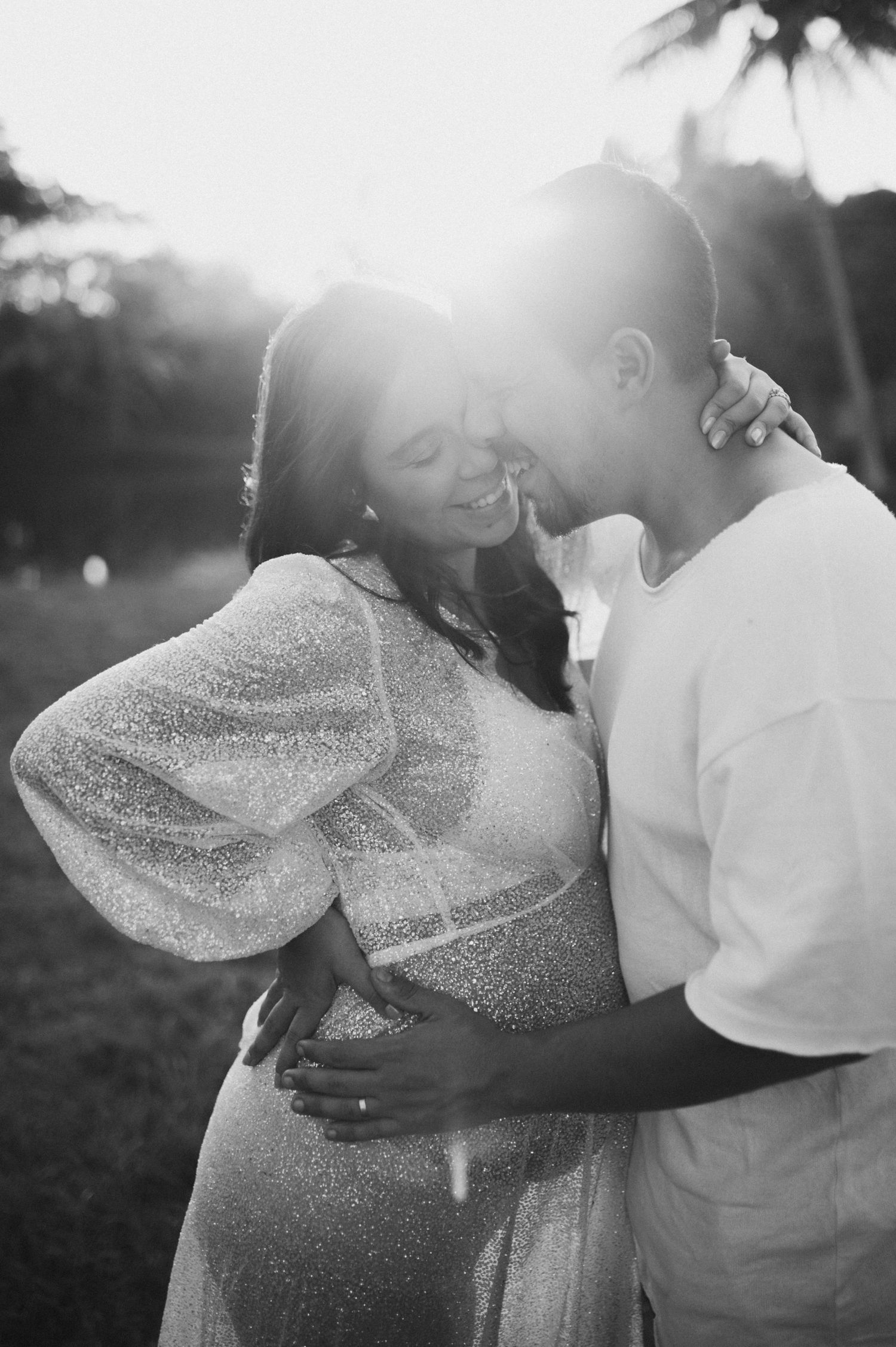 Intimate black and white portrait of couple embracing in sunset light.
