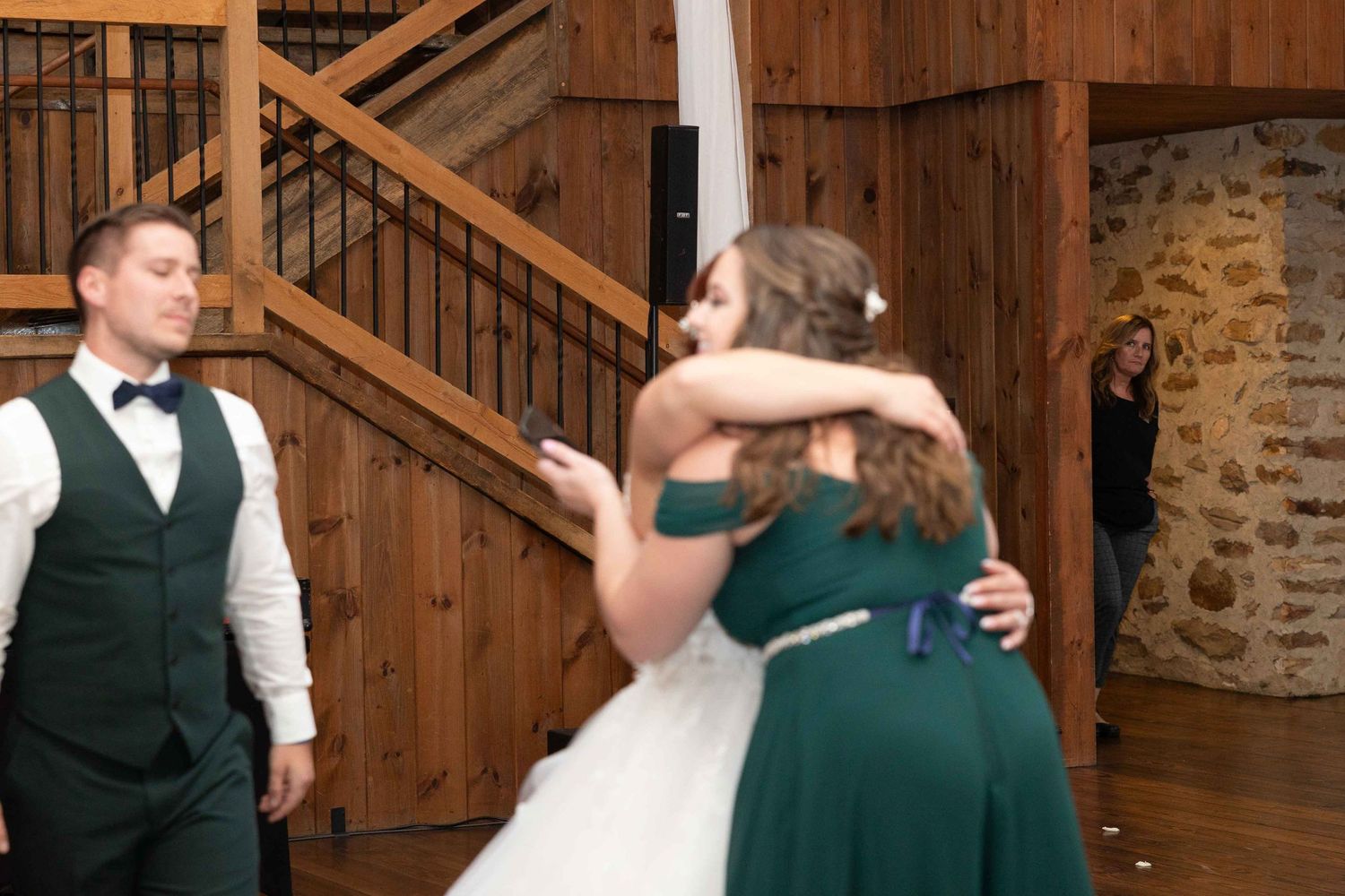 Wedding party members sharing emotional embrace in rustic wooden venue.