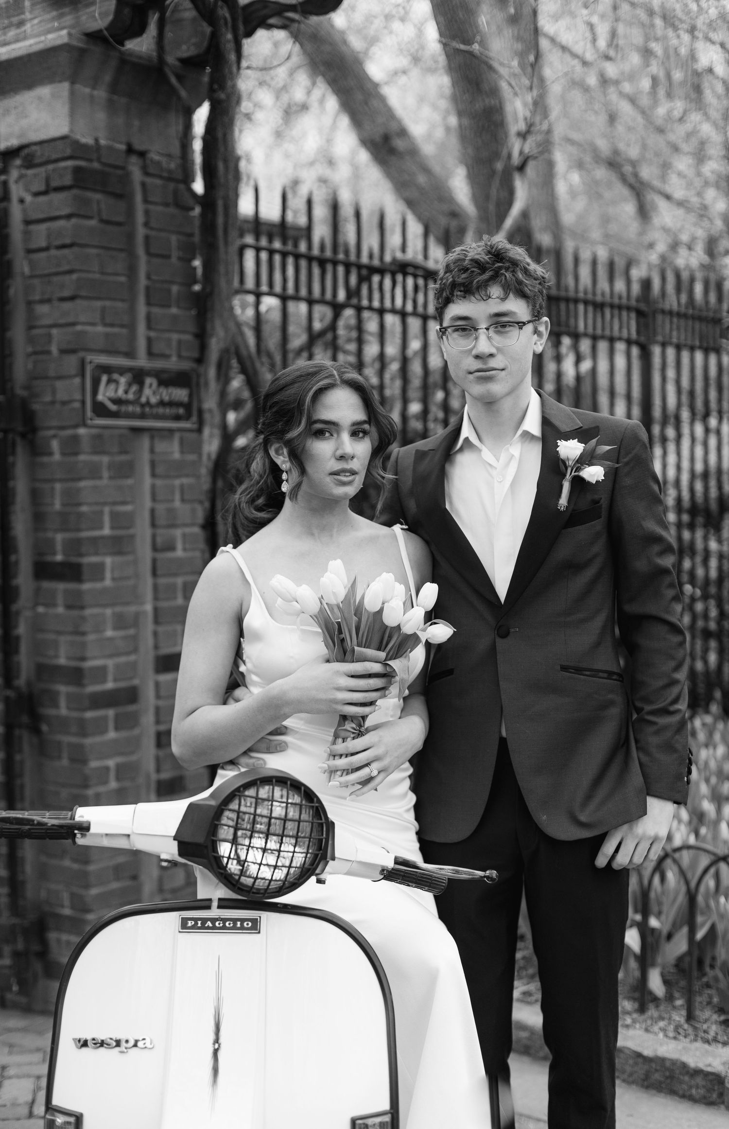 A couple poses with a vintage white Vespa scooter in formal attire.