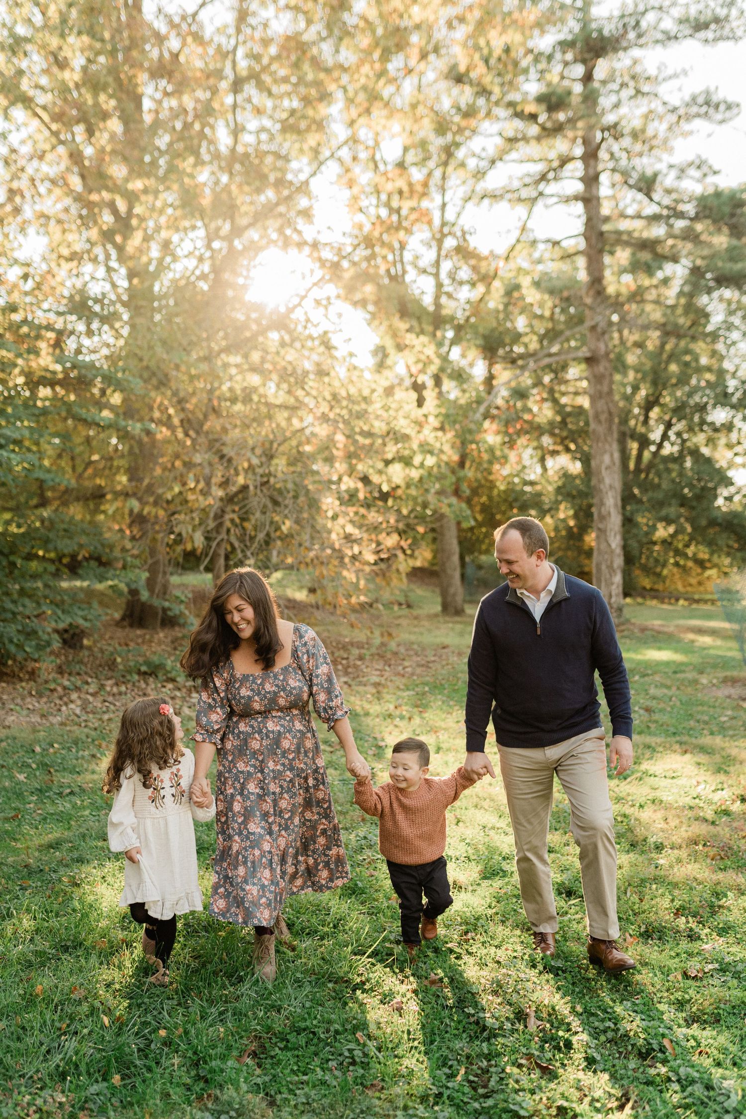 A family walks together holding hands on a sunlit autumn afternoon.