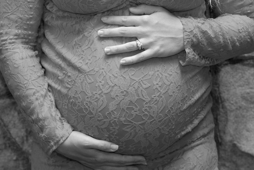 Black and white close-up of hands cradling a pregnant belly through lace fabric.