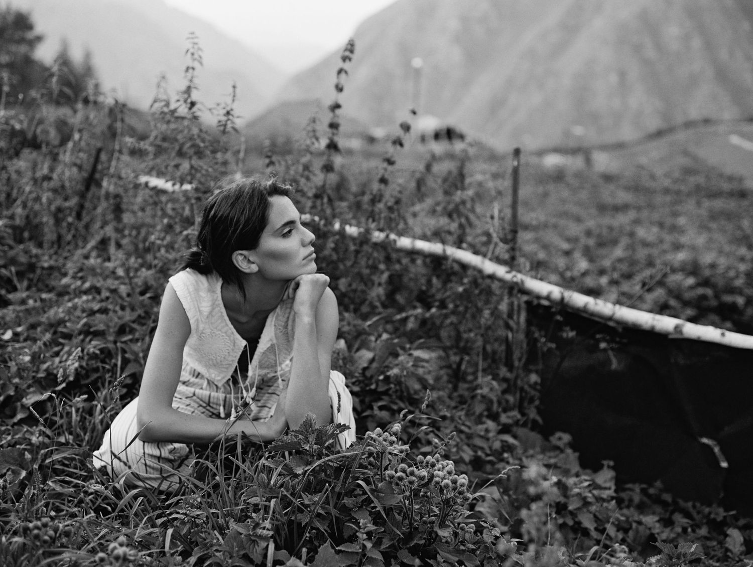 Wearing striped trousers, a woman crouches down in overgrown fields in the mountains of Kazbegi.