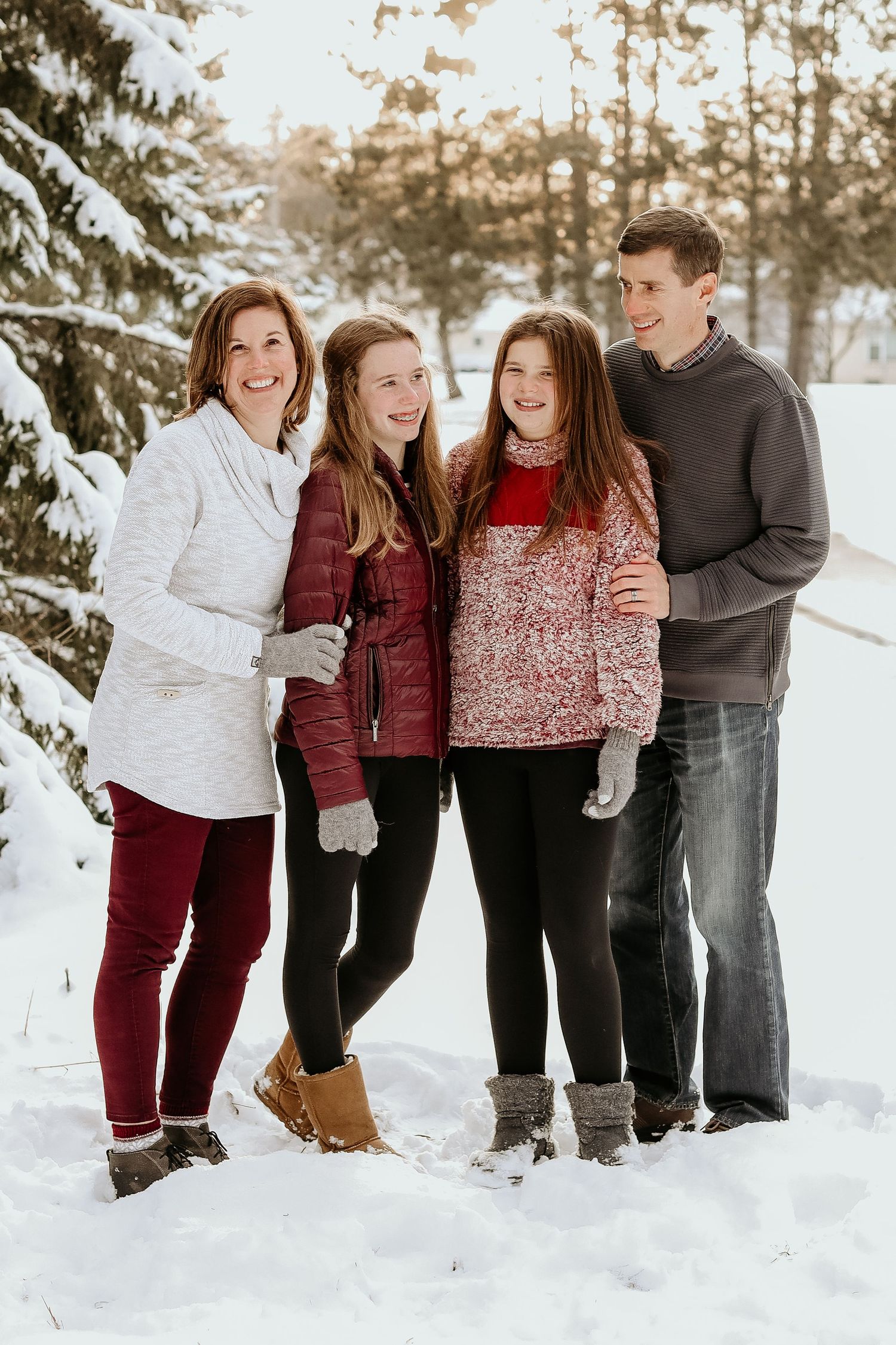Family of four posing together in winter snow scene wearing cozy sweaters.