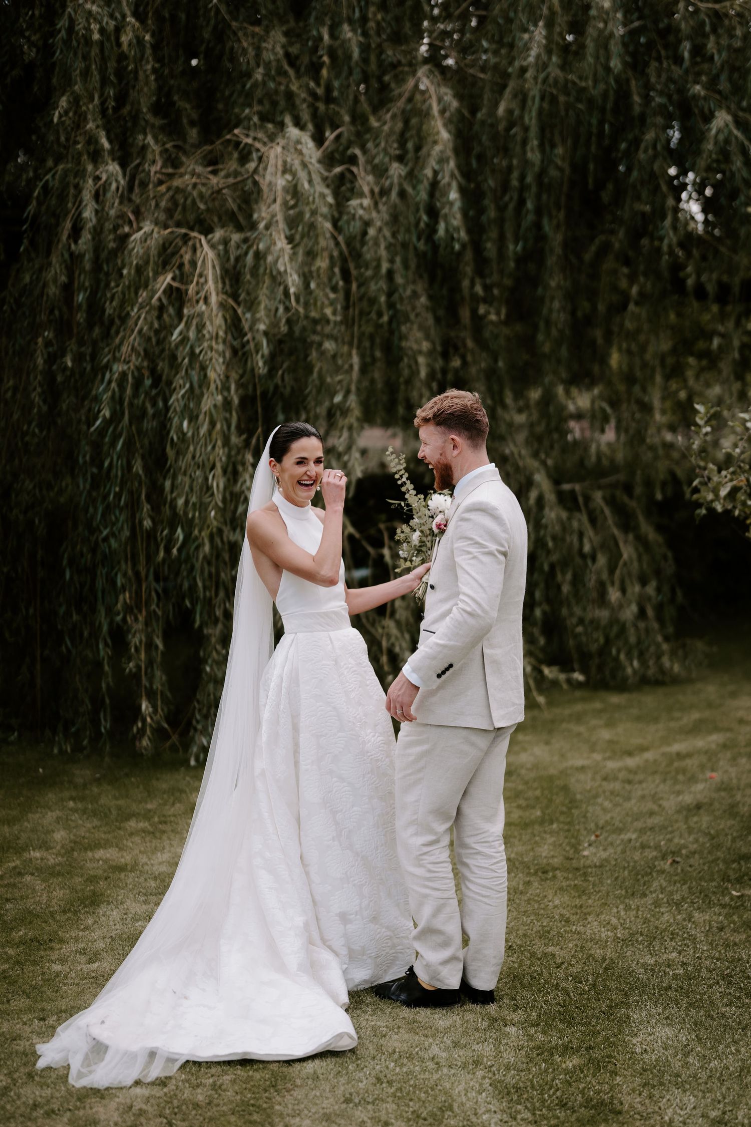 bride and groom stood under a willow tree laughing with each other in islip, Oxfordshire