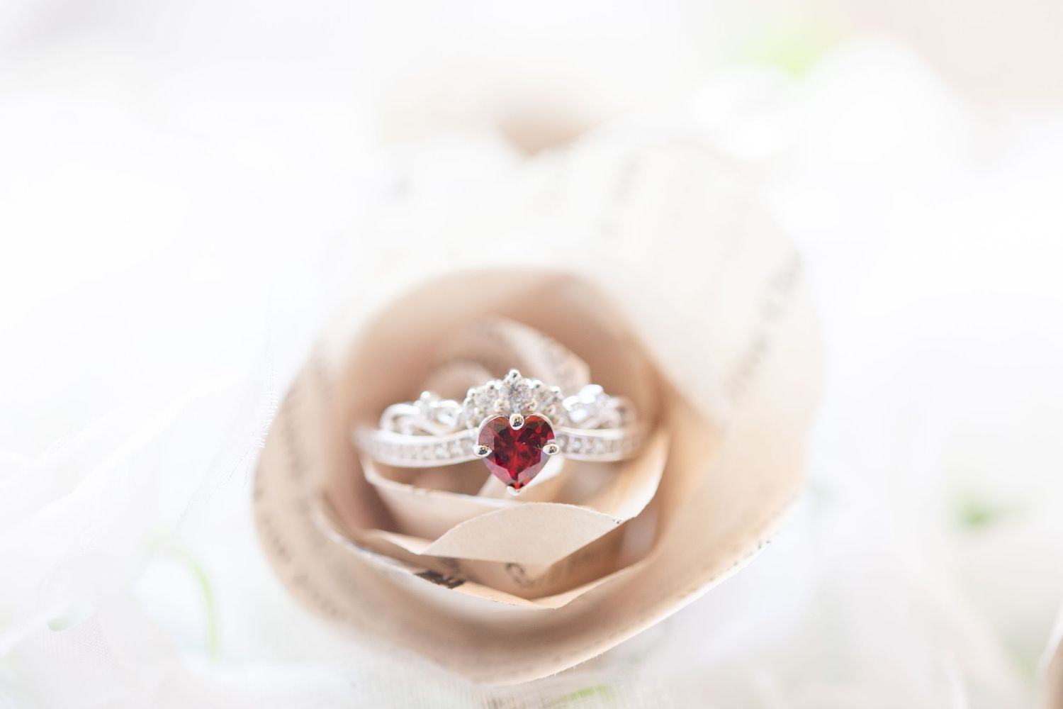 Close-up of an elegant engagement ring with heart-shaped gemstone on soft pink rose petals.