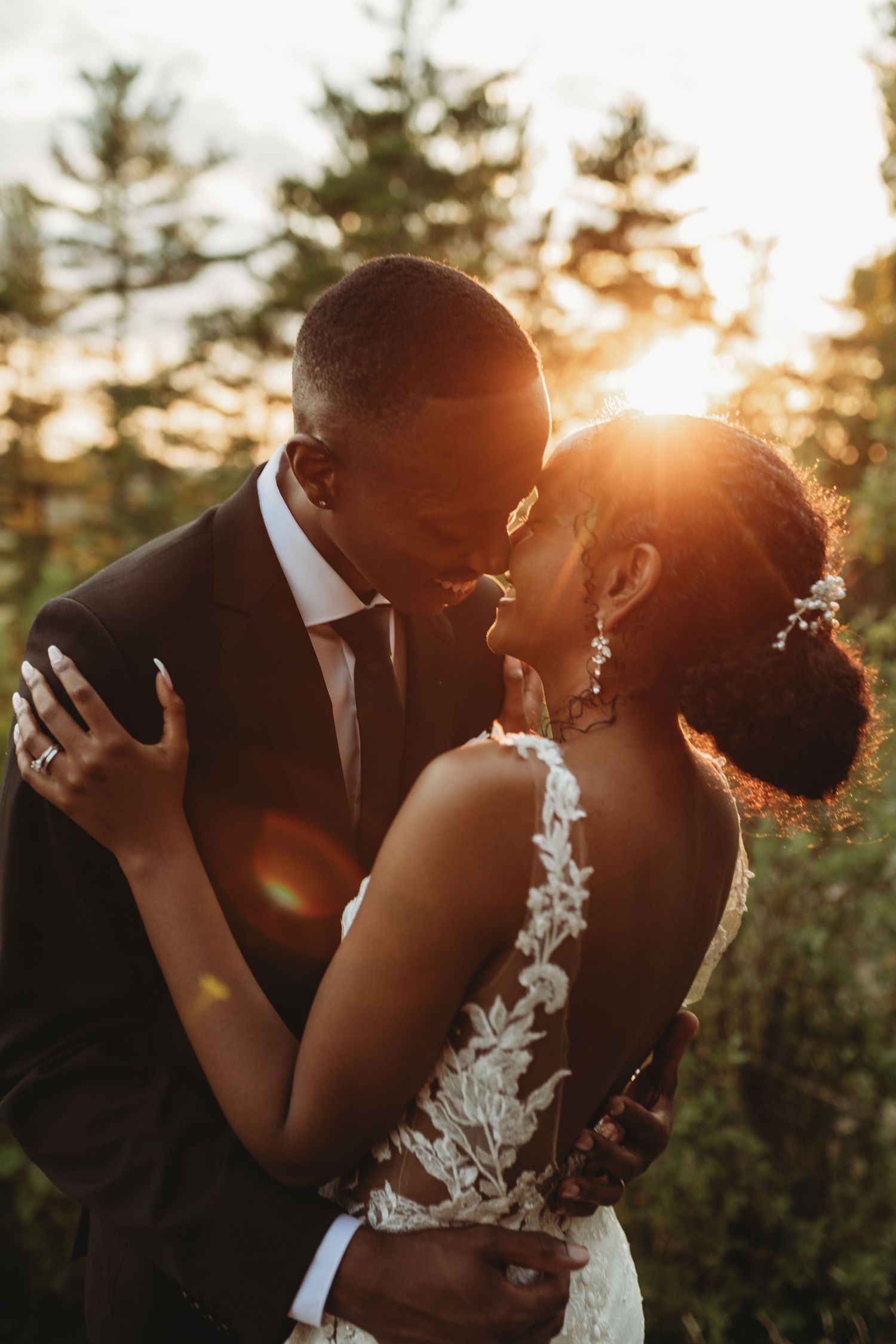 Romantic sunset wedding portrait with lace dress detail and soft golden lighting through pine trees in background.