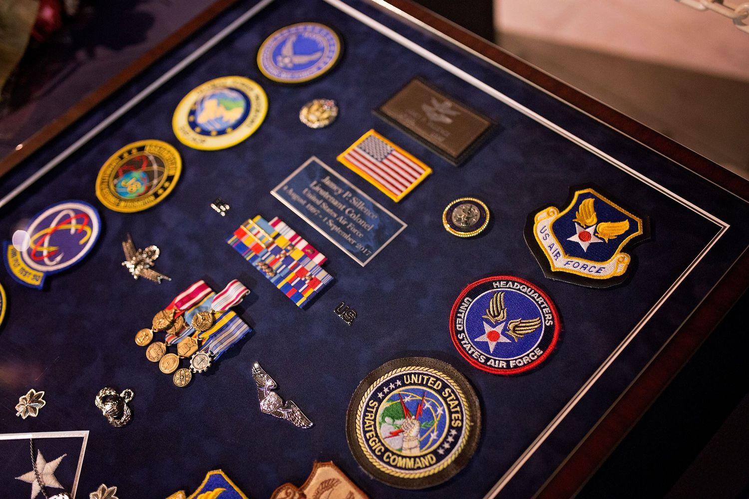 Military patches, medals and insignia displayed on dark blue fabric in a frame.