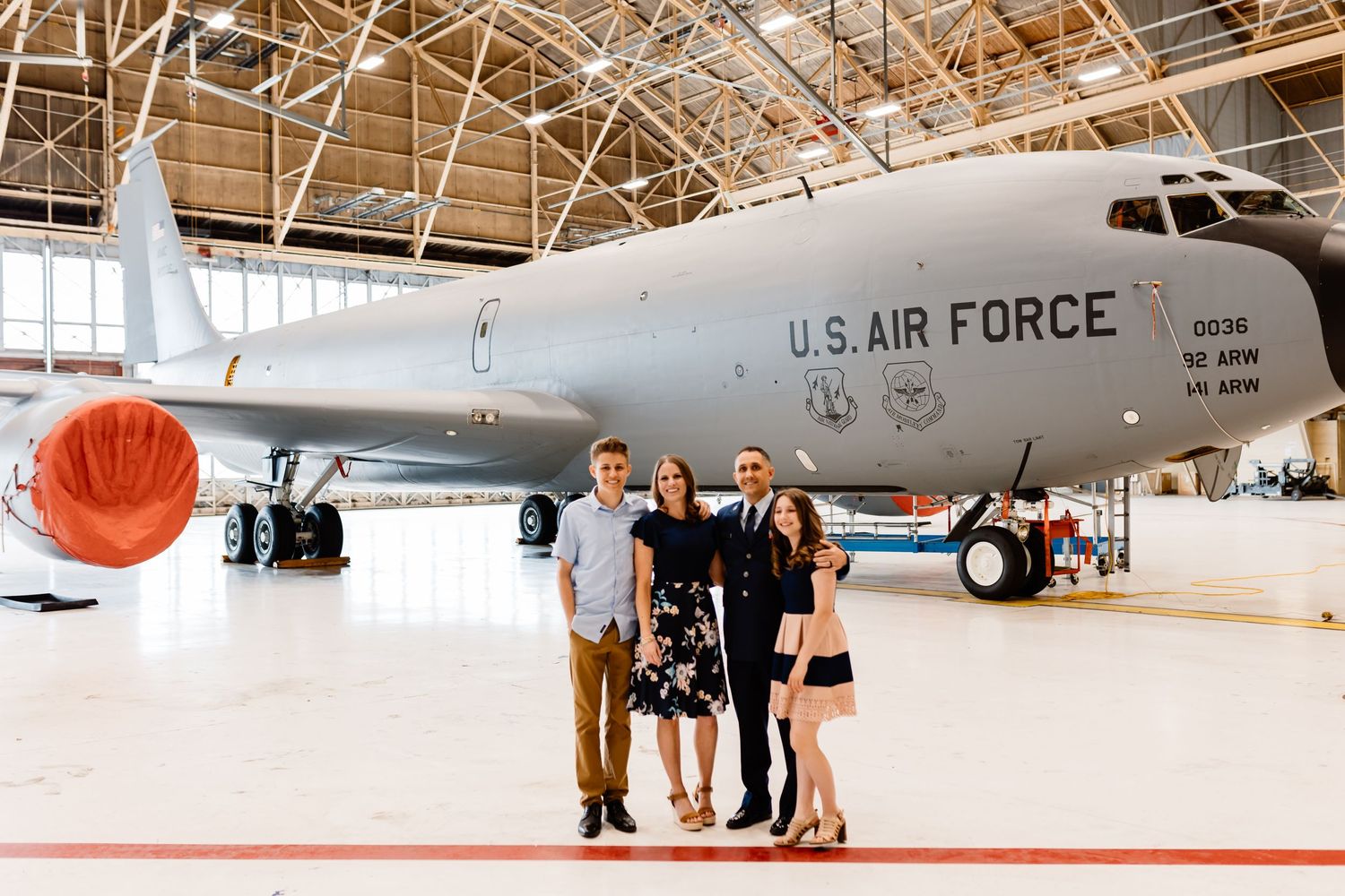 Small group poses together in front of large US Air Force aircraft in hangar.